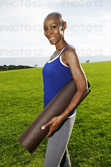 African American woman carrying yoga mat in park