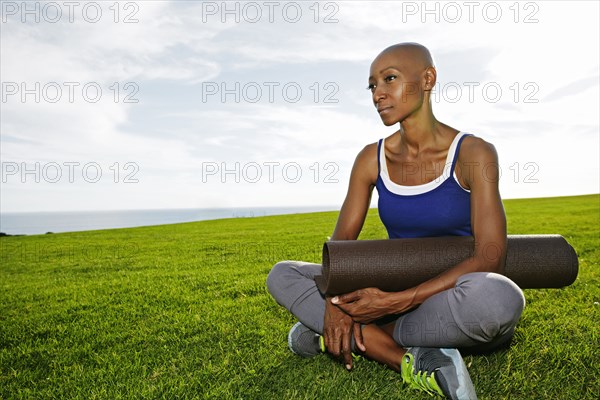 African American woman holding yoga mat in park