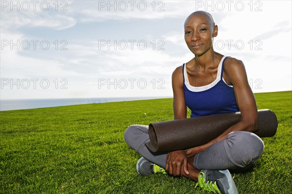 African American woman holding yoga mat in park