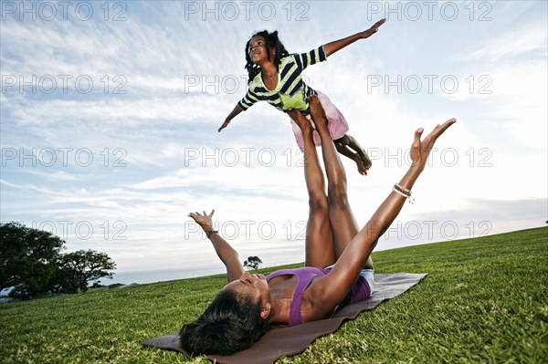 Mother balancing daughter on legs in park