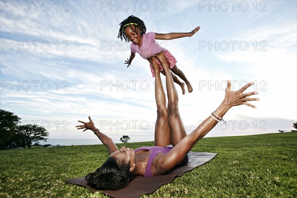 Mother balancing daughter on legs in park