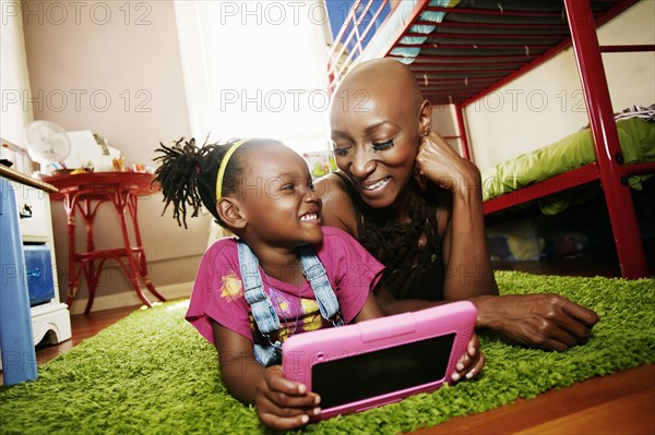 Black mother and daughter using digital tablet in bedroom