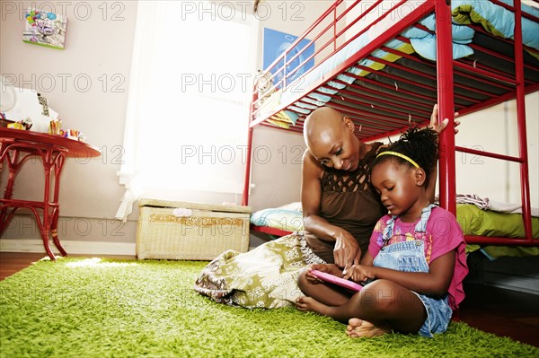 Black mother and daughter using digital tablet in bedroom