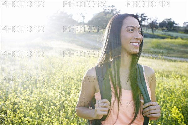 Mixed race woman carrying backpack in field