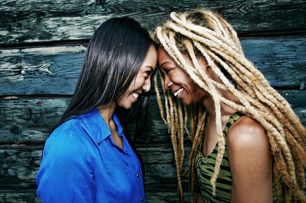 Smiling women touching foreheads at wooden wall