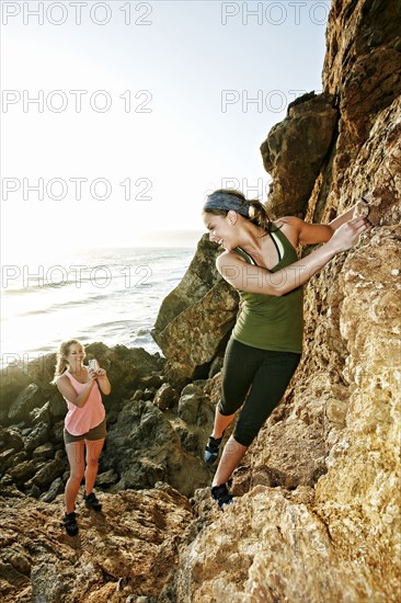 Woman photographing friend climbing rock formation