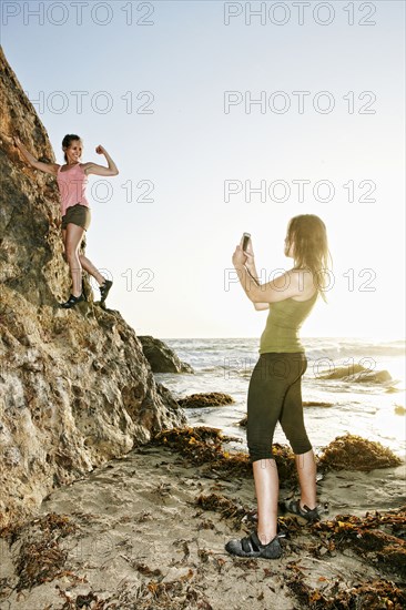 Woman photographing friend climbing rock formation