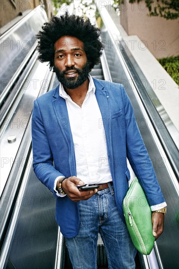 Mixed race businessman using cell phone on escalator