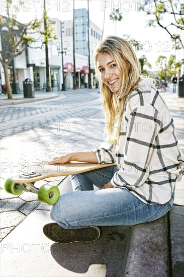 Caucasian woman sitting with skateboard