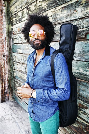 Mixed race musician carrying guitar outdoors