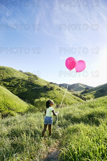 Black girl with balloons on rural hillside