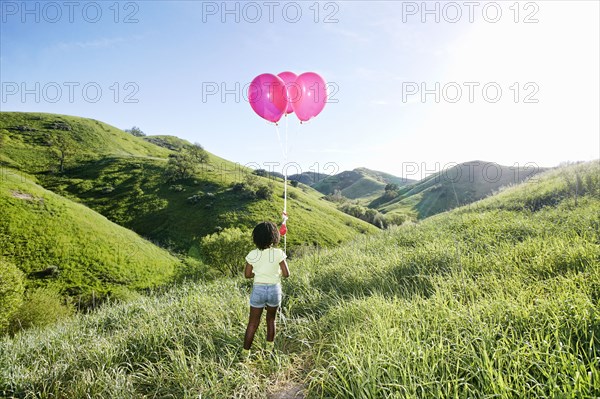 Black girl with balloons on rural hillside