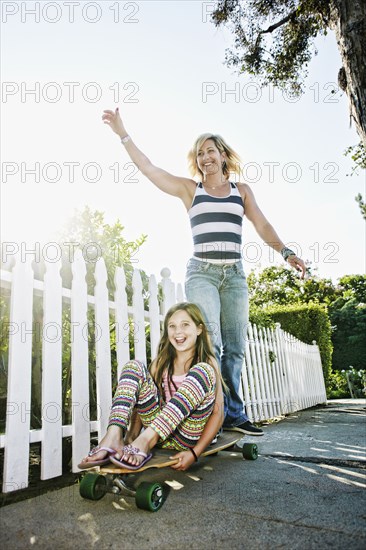 Caucasian mother and daughter riding skateboard on sidewalk