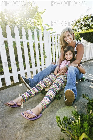 Caucasian mother and daughter riding skateboard on sidewalk