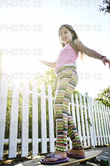 Caucasian girl riding skateboard on sidewalk