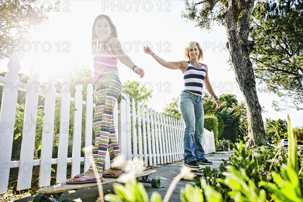 Caucasian mother and daughter riding skateboards on sidewalk