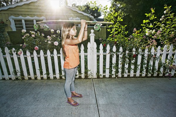 Caucasian girl carrying skateboard on sidewalk