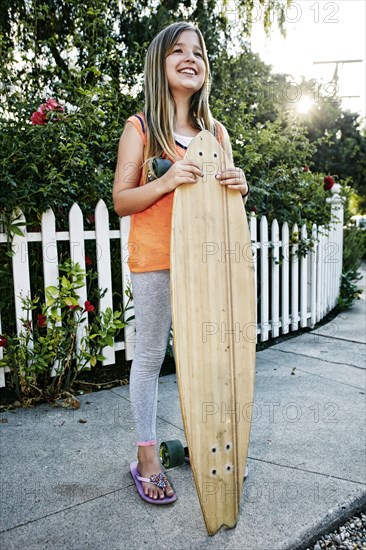 Caucasian girl holding skateboard on sidewalk