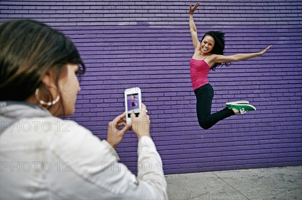 Woman photographing friend jumping for joy