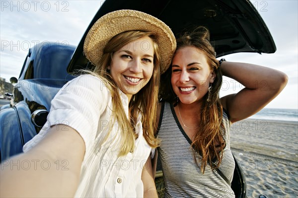 Women taking selfie in vintage car on beach