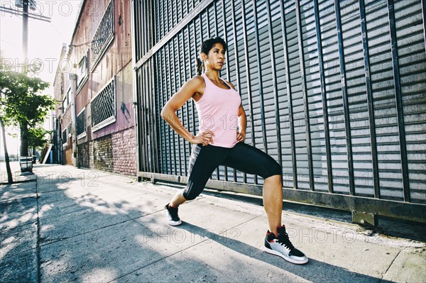 Mixed race woman stretching on sidewalk