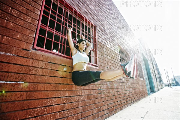 Mixed race woman doing pull-ups on window grate