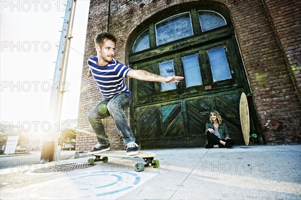 Caucasian man riding skateboard on sidewalk