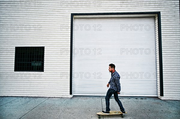 Caucasian man riding skateboard on sidewalk