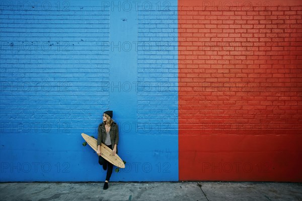 Caucasian woman holding skateboard at painted wall