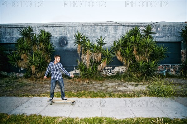 Caucasian man riding skateboard on sidewalk