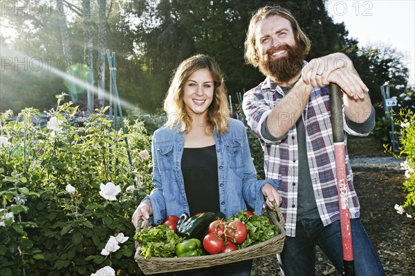 Couple standing with basket of vegetables in garden