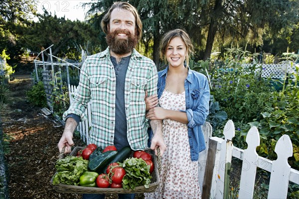 Couple standing with basket of vegetables in garden