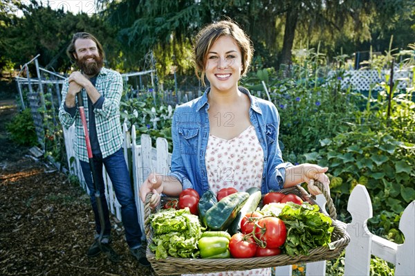 Couple standing with basket of vegetables in garden