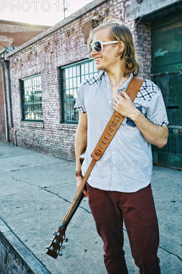 Caucasian man carrying guitar outdoors