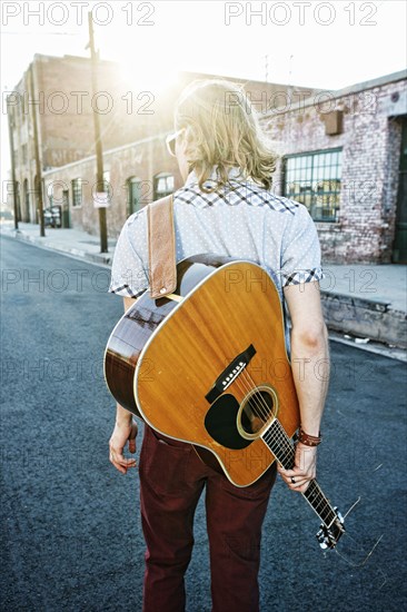 Caucasian man carrying guitar outdoors