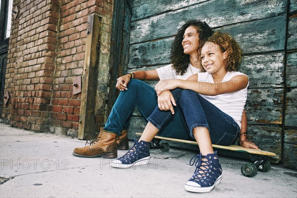 Mixed race mother and daughter sitting on skateboard