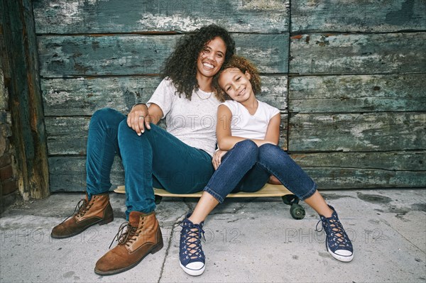 Mixed race mother and daughter sitting on skateboard