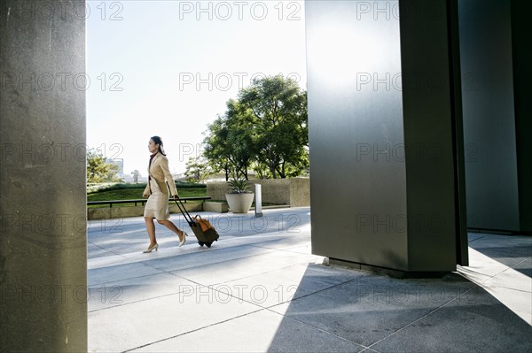 Asian businesswoman rolling luggage outdoors