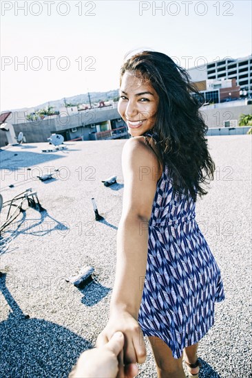 Hispanic woman pulling hand on urban rooftop