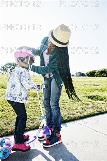 Black mother fastening helmet on daughter