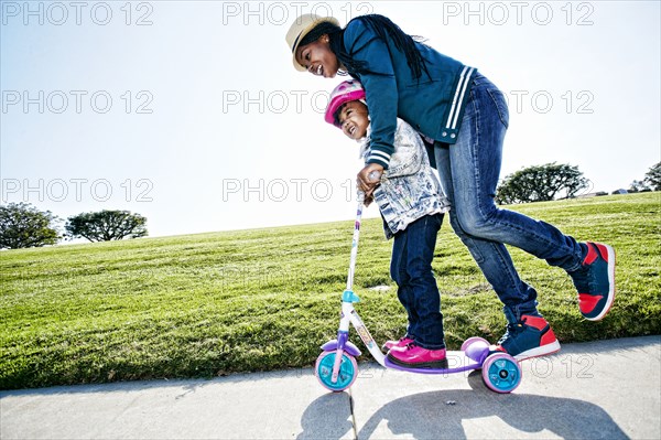 Black mother and daughter riding scooter