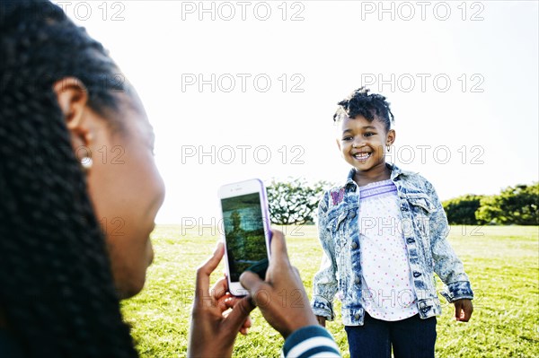 Black mother photographing daughter outdoors