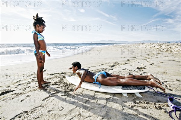 Black mother teaching daughter to surf on beach