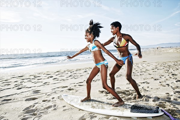 Black mother teaching daughter to surf on beach