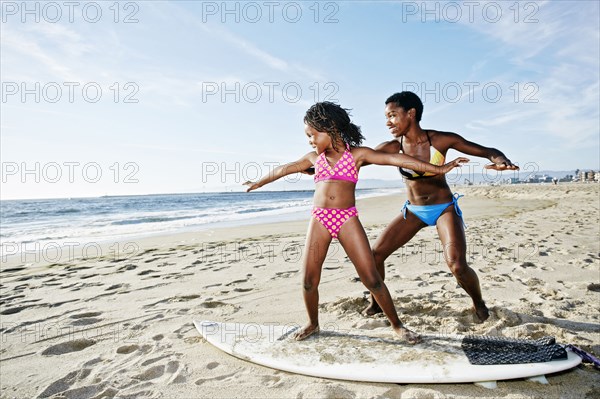 Black mother teaching daughter to surf on beach