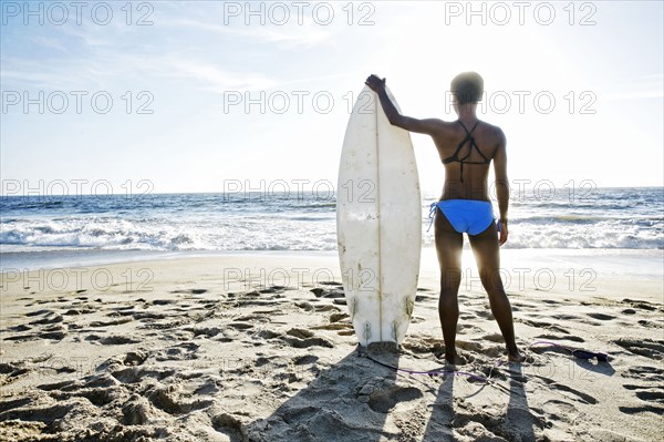 Black woman carrying surfboard on beach