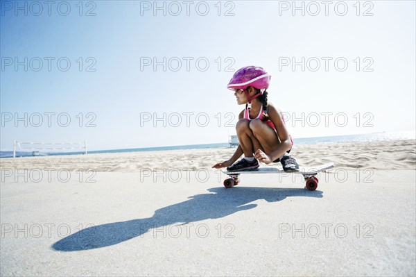 Mixed race girl riding skateboard at beach