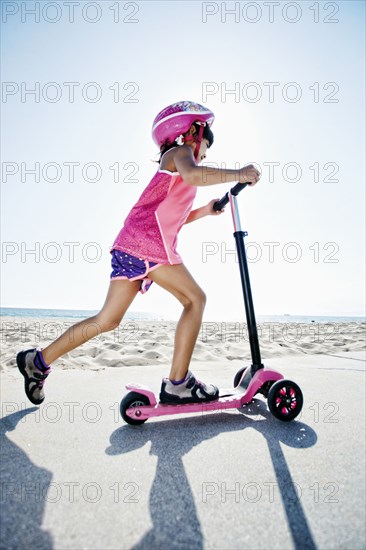 Mixed race girl riding scooter at beach