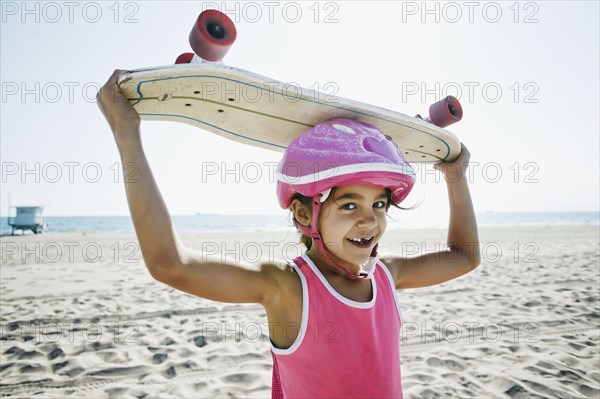 Mixed race girl holding skateboard at beach