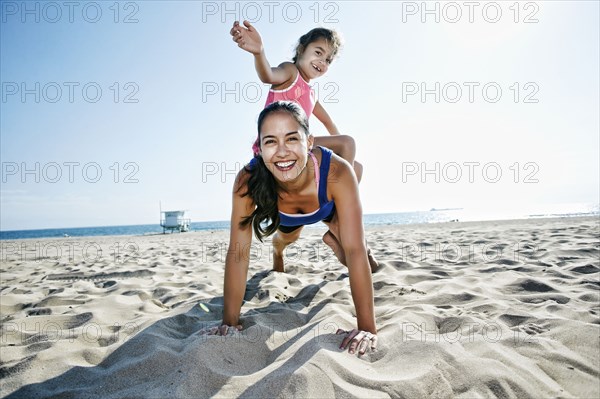 Mother doing push-ups with daughter at beach